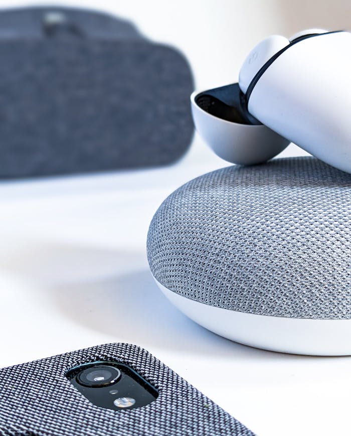 hero-gallery-02 Close-up of wireless earbuds, smartphone, and smart speaker illustrating contemporary tech design.