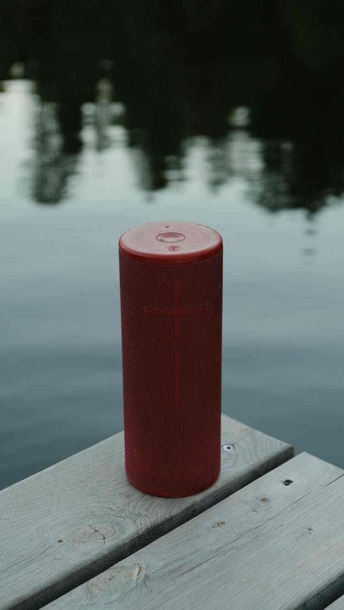 hero-gallery-01 Red wireless speaker on a wooden dock by a serene lake. Ideal for outdoor music.